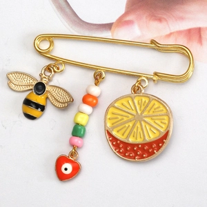 Macro detail of a gold pin with bee, heart beads, and lemon charms on light background