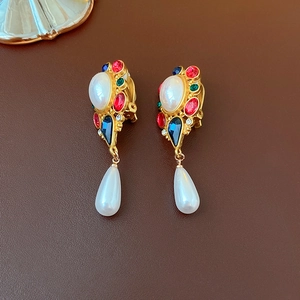 Close-up of vintage gold earrings with pearls, colorful gems on brown leather background