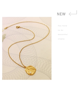 Detail of gold pendant necklace with irregular shell texture and white pearl accent