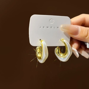 Close-up of elegant C-shaped gold and pearl earrings held on a professional card
