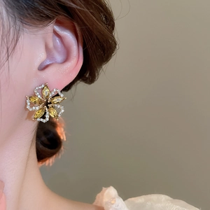 Detailed view of irregular flower earring with yellow gemstones on model's ear
