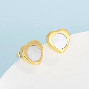 Vue macro de boucles d'oreilles cœur dorées avec incrustation blanche sur fond bleu