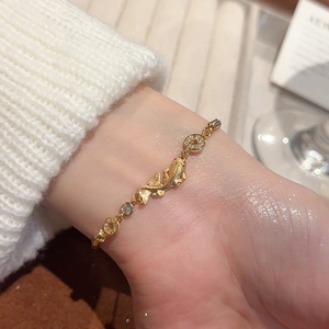 Close-up of golden carp and coin charms bracelet with zircon inlay on female wrist