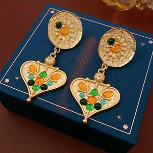 Macro shot of vintage gold heart earrings with green and orange gemstones on navy jewelry box