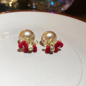 Close-up of pearl stud earrings with red flocked dog pendants on a white ceramic tray