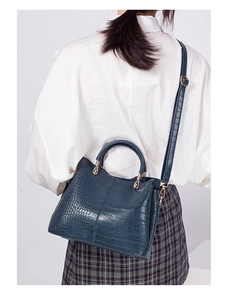 Detail of dark blue crocodile pattern handbag with gold hardware on a model