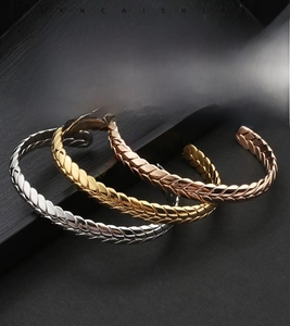 Detail of three wheat-ear pattern stainless steel open bracelets in gold, silver, and rose gold