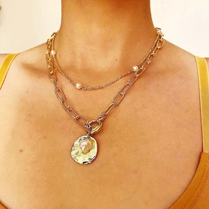 Detail of layered gold chain necklace featuring baroque pearls and irregular pendant