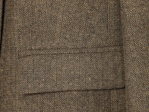 Detail of herringbone pattern tweed jacket showing fabric texture and pocket flap