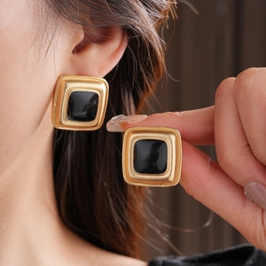Close-up of vintage style golden square earrings with black enamel inlay on model