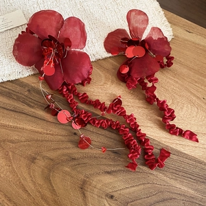 Macro view of red fabric flower earrings with sparkling sequins and long tassel ribbons