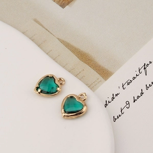 Détail de deux pendentifs cœur en cristal vert avec monture dorée posés sur un livre