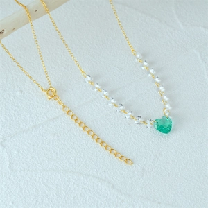 Close-up of a gold necklace with a green heart gemstone pendant on a rustic wood background