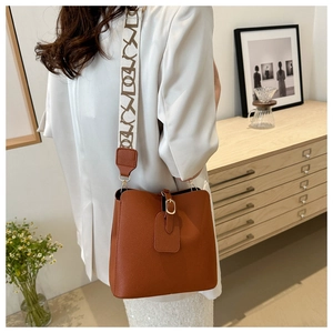 Brown litchi leather bucket bag shown on a model with a wide patterned fabric strap