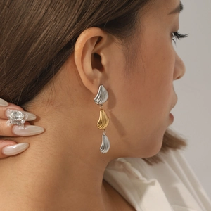 Close-up of model wearing three-tier shell leaf drop earrings in gold and silver finish