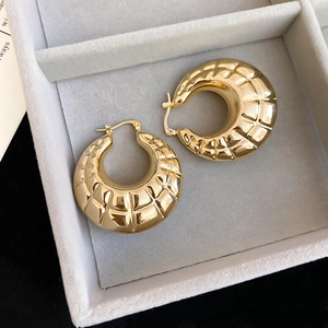 Detail of golden chunky hoop earrings with quilted texture in a gray jewelry box