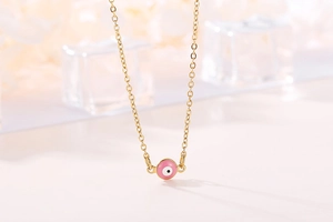 Macro shot of pink enamel evil eye pendant on a delicate gold stainless steel chain