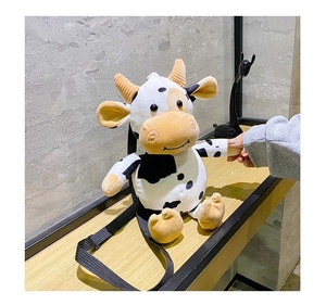 Detail showing plush cow crossbody bag with black spots and yellow horns on wood table