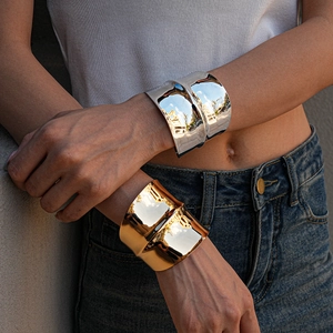 Close-up of wide mirror-finish metal bangles with liquid flowing texture in gold and silver