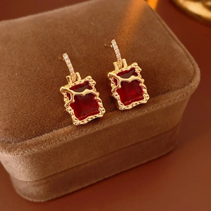 Gros plan de boucles d'oreilles dorées carrées avec pierre rouge sur boîte bijoux