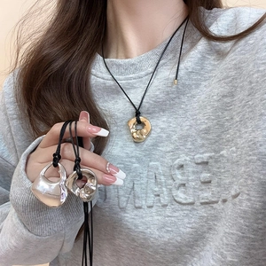Detail of hollow heart and liquid metal pendants on black wax cords worn by a model