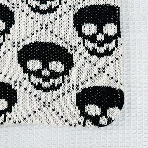 Close-up detail of knitted fabric with black and white skull patterns and soft texture
