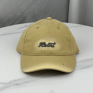 Detailed embroidery of Heart text on mustard yellow baseball cap with distressed hole design