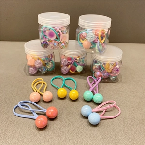 Close-up of colorful candy-colored ball hair ties in jars on a textured grey surface