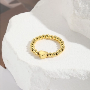 Detailed view of a gold beaded elastic ring with a heart charm on a stone background