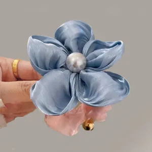 Macro detail of a blue satin flower hair tie with pearl center held by hand