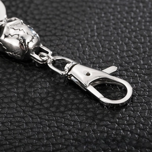 Close-up of silver skull keychain with lobster clasp on black leather background