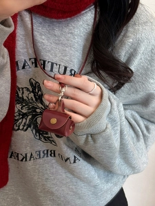 Close-up of burgundy leather coin pouch necklace with button snap on grey sweatshirt