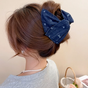 Detail of dark blue denim bow hair claw clip worn on an elegant braided hairstyle