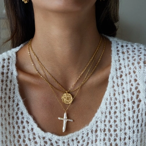 Detail of layered gold coin necklace with cross and pearl pendant on a model