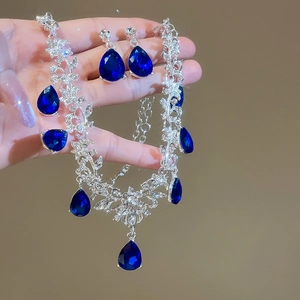 Close-up of elegant silver necklace and earrings with dark blue teardrop pendants