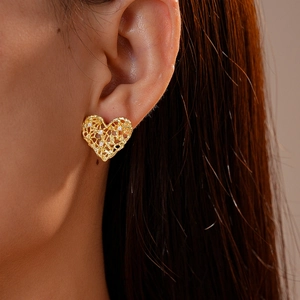 Close-up of heart-shaped hollow gold earrings with zircon stones on a female model