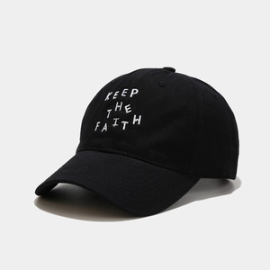 Close-up of white KEEP THE FAITH embroidery on a black cotton baseball cap surface