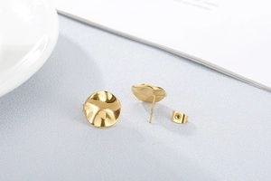 Detailed view of gold irregular wavy earrings with hammer texture on a textured background