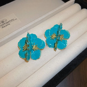 Détail de boucles d'oreilles fleur en émail bleu avec pistils dorés dans un écrin