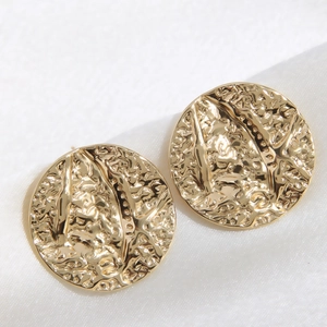 Close-up of golden round stud earrings with hammered metal texture on white silk fabric