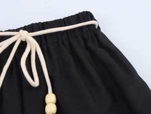 Dettaglio dei pantaloni neri con elastico in vita e cordino intrecciato con perline in legno
