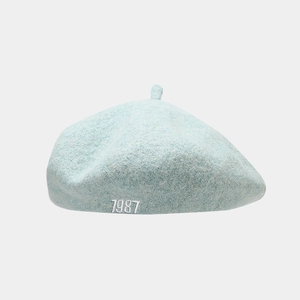 Close-up of mint blue beret featuring white 1987 embroidery and soft wool texture
