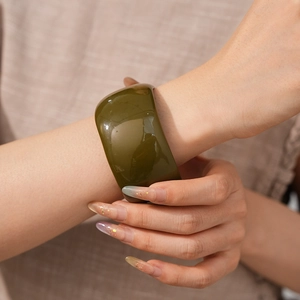 Detail view of olive green resin wide bangle bracelet worn on wrist with natural fabric