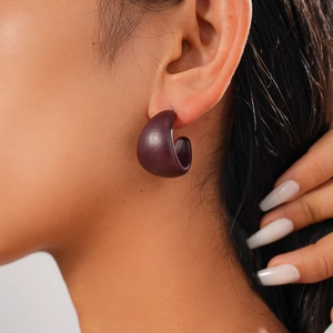 Detail shot of a dark purple matte C-shaped geometric earring worn on a model ear
