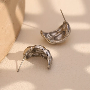 Macro shot of silver woven horn stud earrings with polished metallic texture and waves