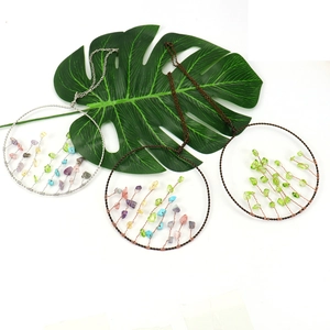 Detailed wire-wrapped Tree of Life pendants with colorful crystals on tropical green leaves