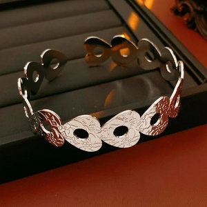 Macro detail of silver open cuff bracelet featuring heart cut-outs and floral relief