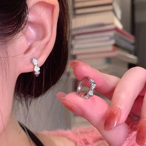 Detail of silver bow huggie earrings with micro-set zircon stones on the earlobes