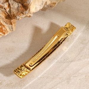 Golden stainless steel hair clip with textured metal finish on marble stone background