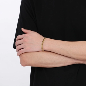 Detail of a gold curb chain bracelet on a male wrist showing the polished metal links
